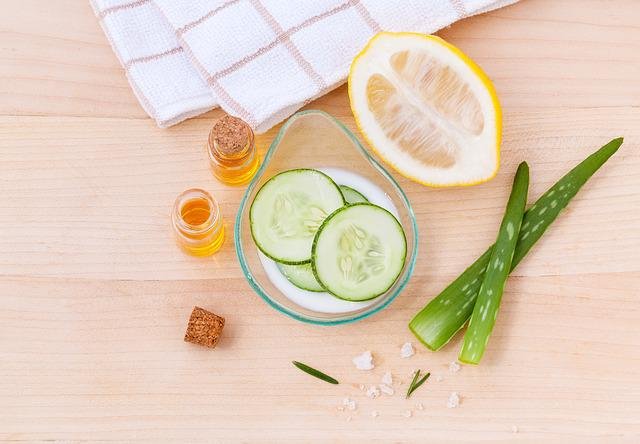 Cucumber, essential oils, aloe, and sea salt skincare ingredients on a wooden table next to a towel.