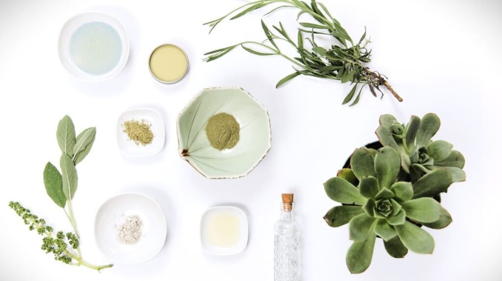 Natural wellness ingredients on a white table. Powders, plants, bowl, glass bottle.