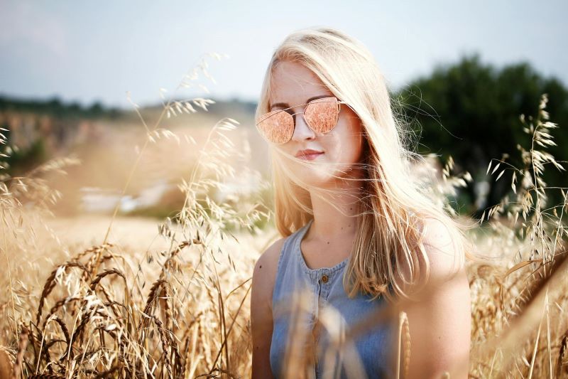 Young blonde women with sunglasses standing in the sunlight in a wheat field.